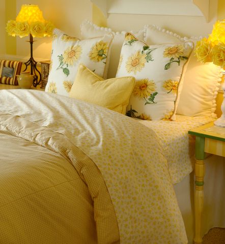 a bed with yellow and white pillows on top of it next to a night stand