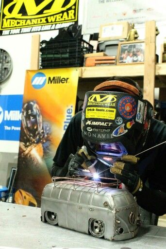 a man welding something on top of a piece of metal in a shop with other items