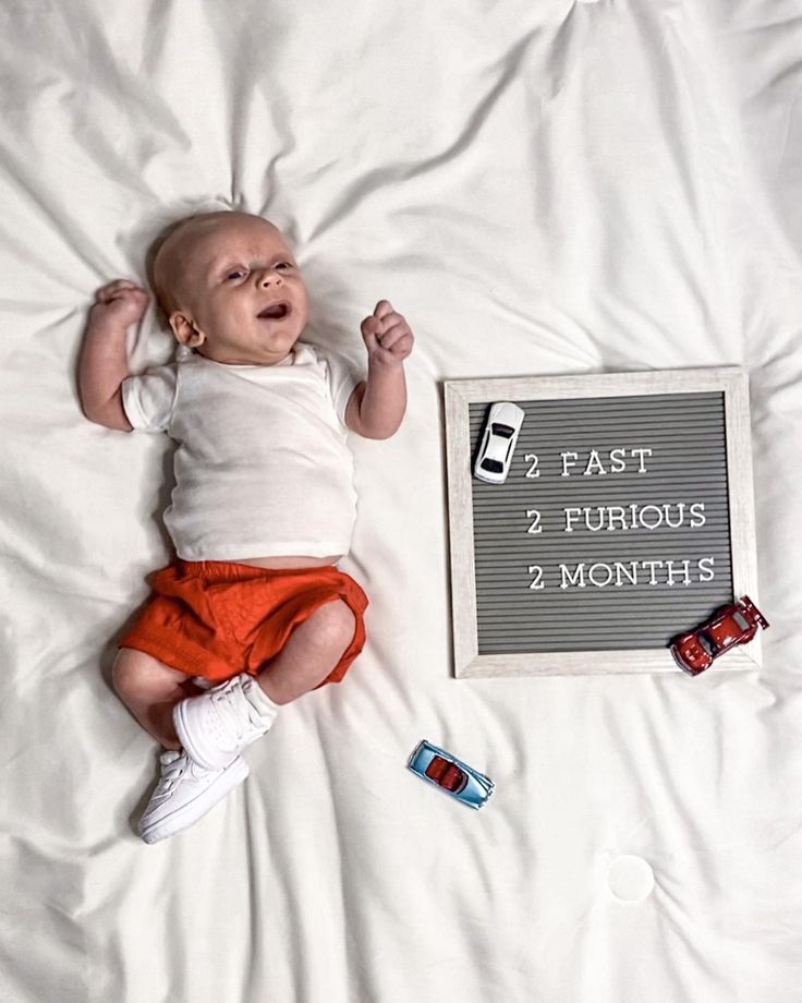 a baby laying on top of a bed next to a sign that says fast, 2 furious 3 months