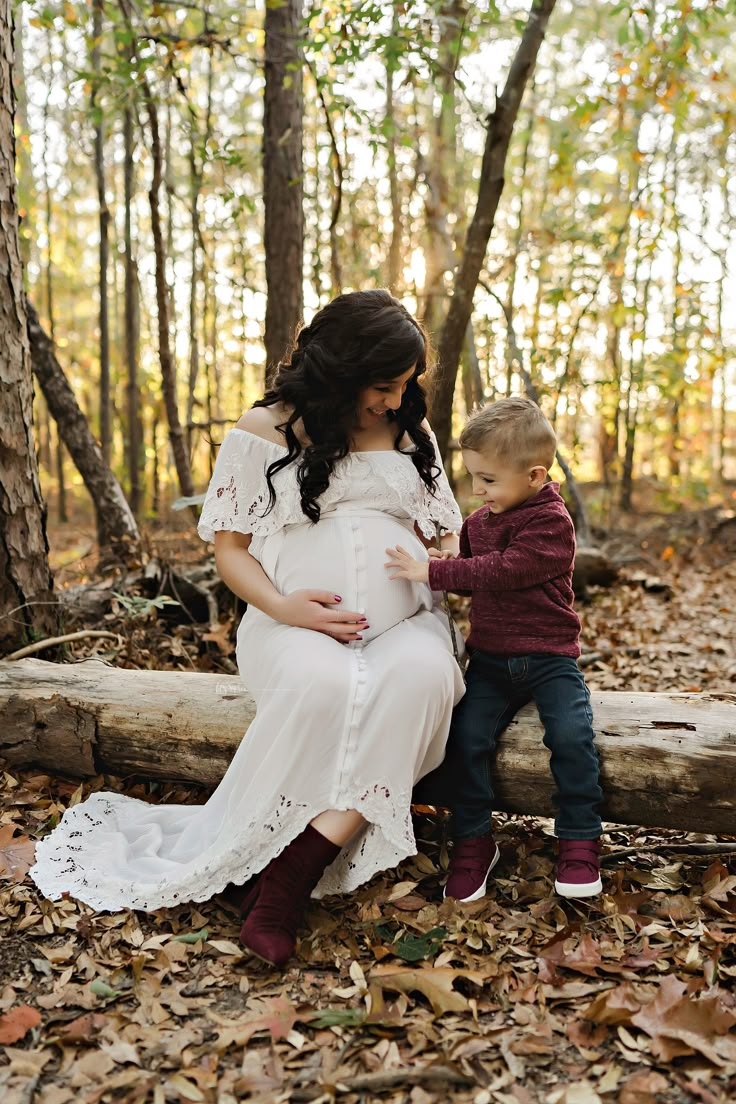 a pregnant woman sitting next to a little boy in the woods