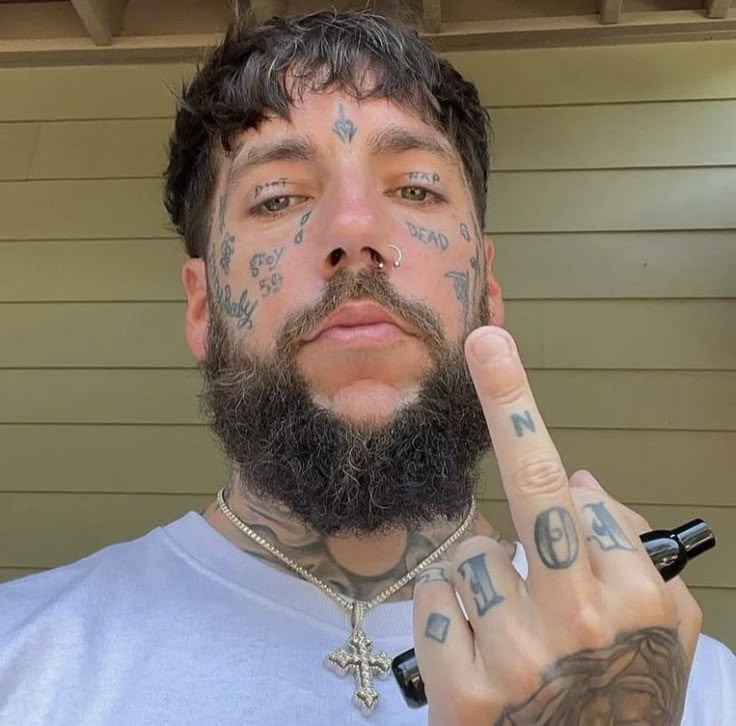 a man with tattoos on his face and fingers making the peace sign while standing in front of a house