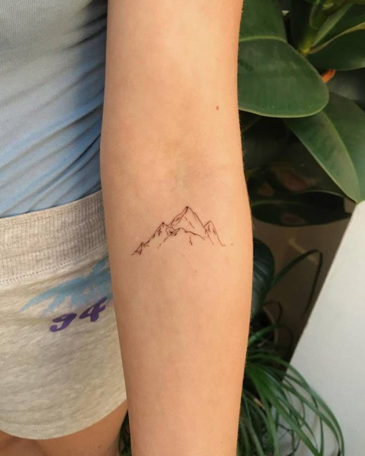 a woman's arm with a small mountain tattoo on the left side of her arm