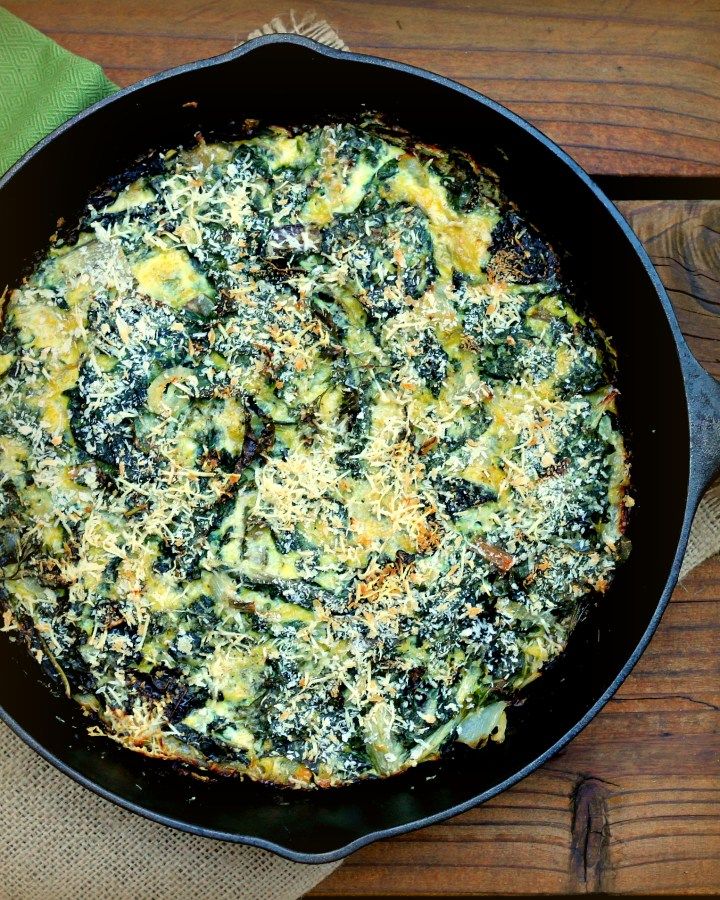 an omelet with spinach and cheese in a skillet on a wooden table