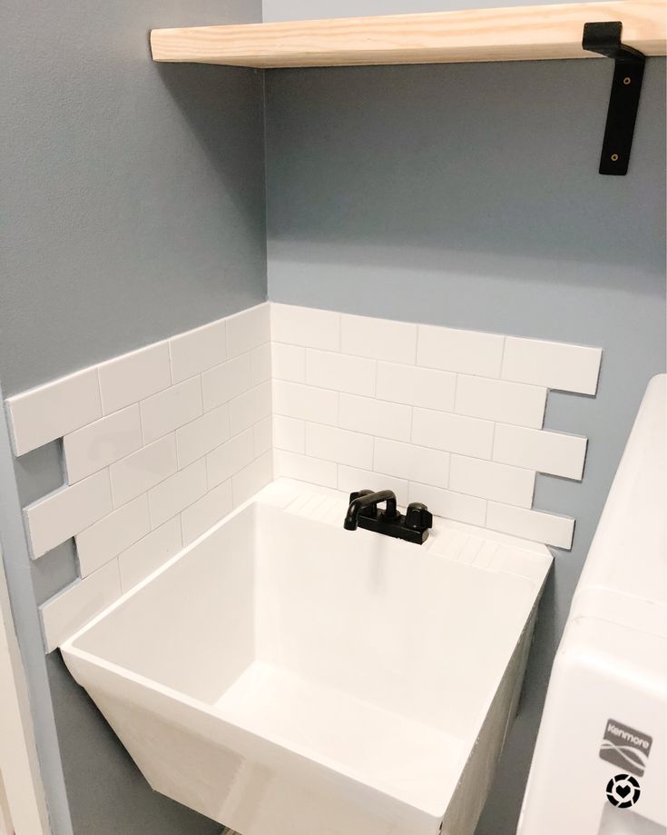 a bathroom with a white sink and black faucet next to a shelf on the wall