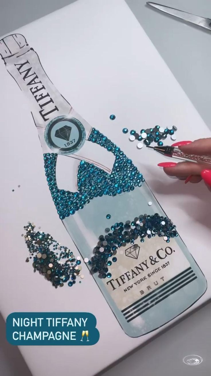 a woman is painting a bottle with blue and silver glitters on the side of it