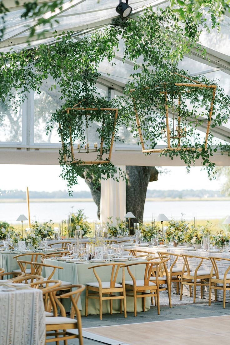 the tables are set up for an outdoor wedding reception with greenery hanging from the ceiling