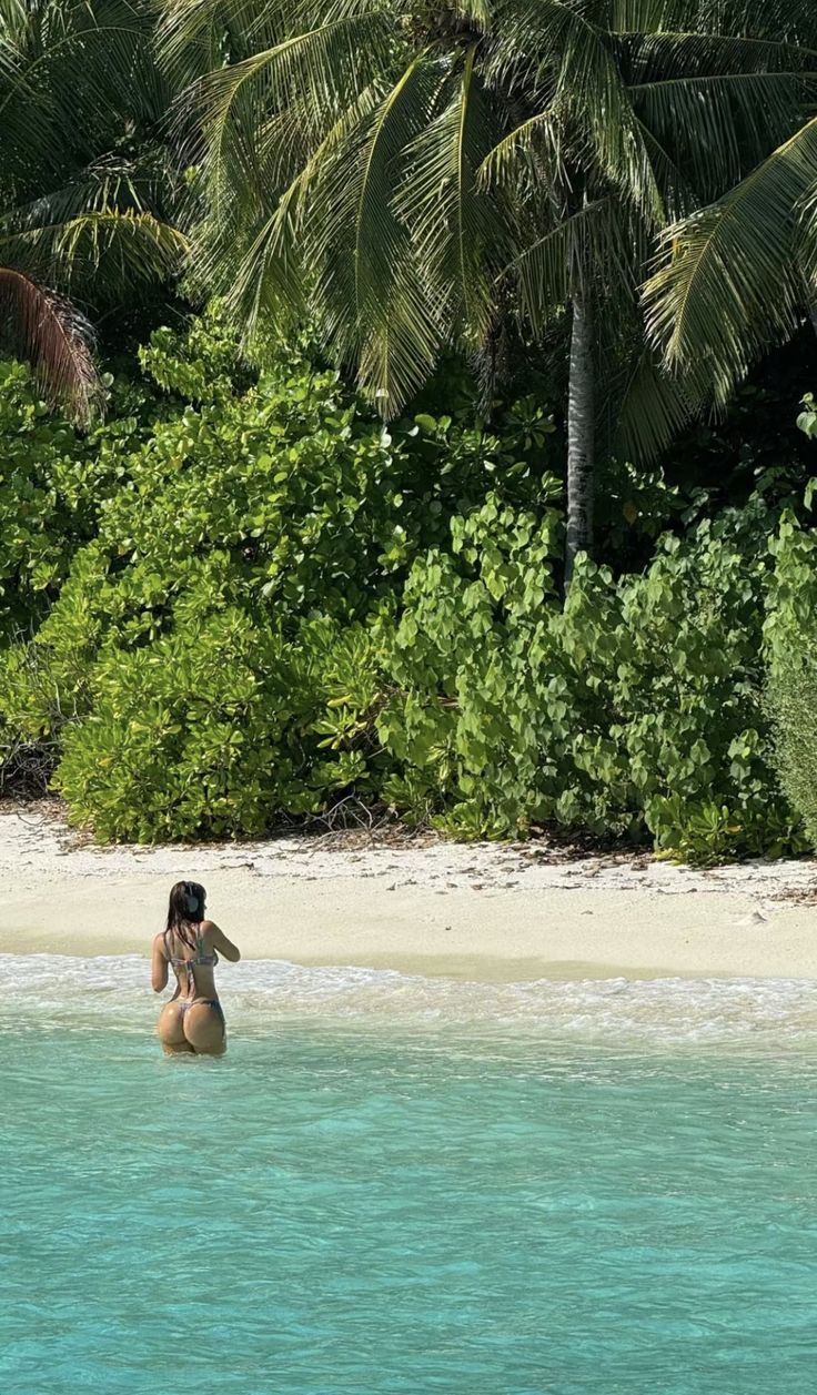 a woman is standing in the water with her back turned to the camera and looking at the beach