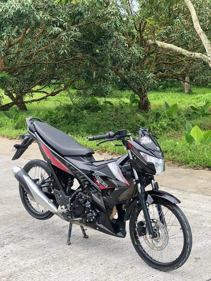 the motorcycle is parked on the side of the road in front of some green trees