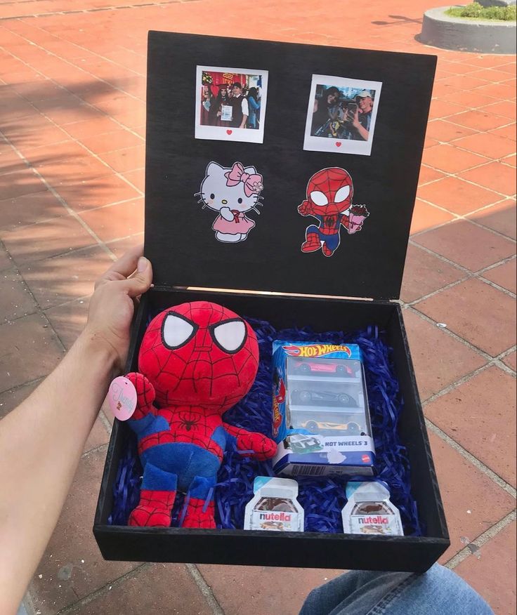 someone is holding up a spiderman stuffed animal in a box with pictures on it