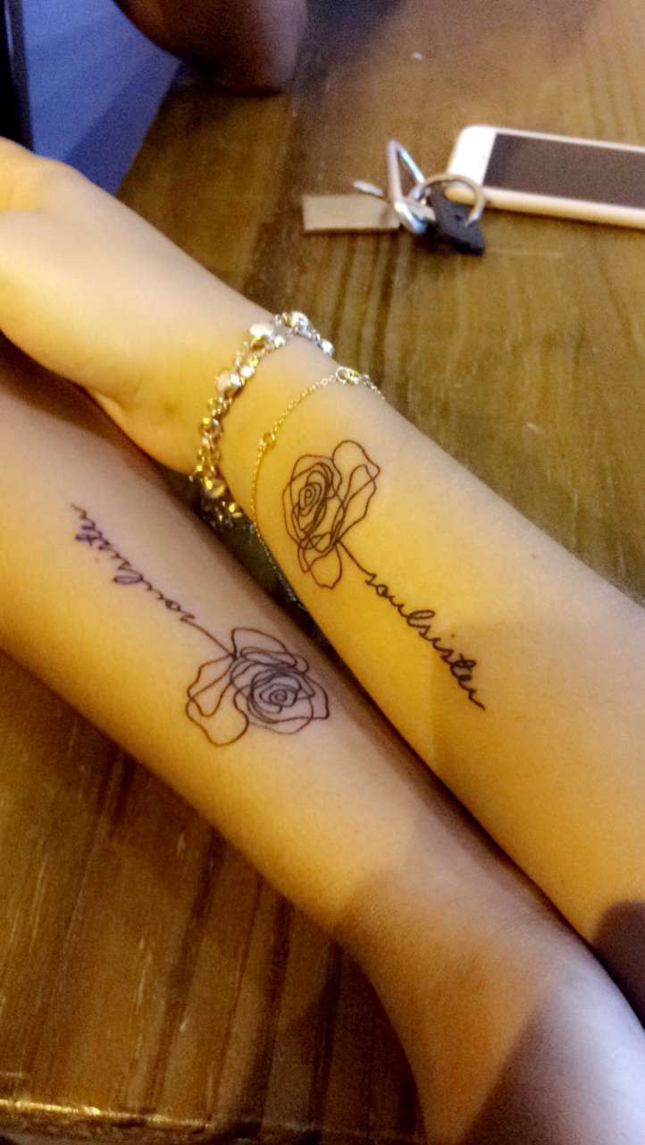 two people sitting at a table with tattoos on their arm and wrist, one is holding the other's hand