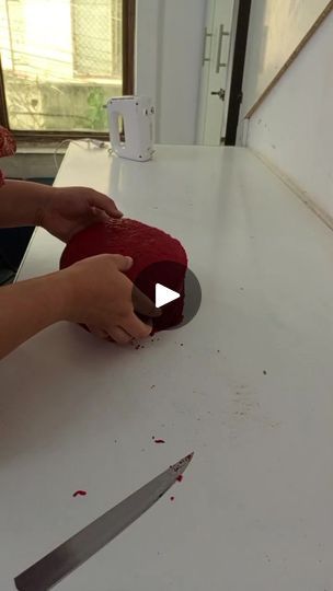 a person cutting up a red hat on top of a white table with a knife