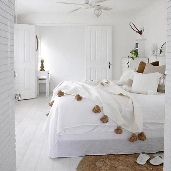 a bedroom with white walls and flooring has a bed covered in blankets, pom - poms