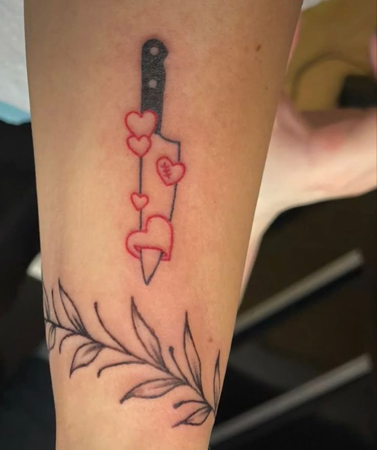 a tattoo on the leg of a woman with a knife and hearts attached to it