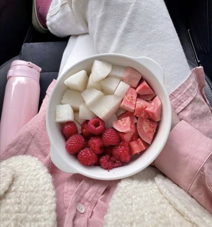 a white bowl filled with fruit on top of a bed next to a pink blanket