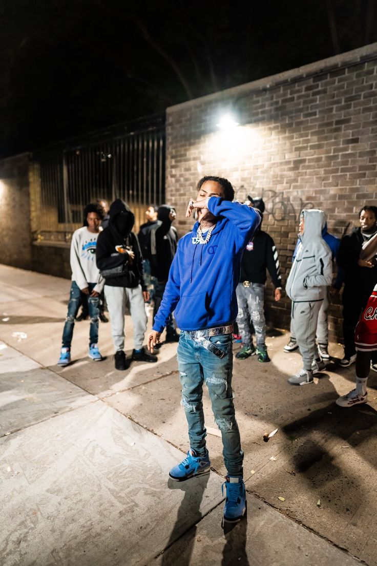 a man standing on the sidewalk talking on his cell phone while wearing a blue hoodie