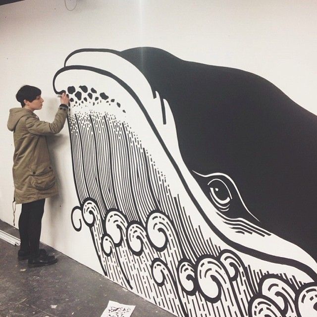 a man is painting a mural on the side of a wall with black and white designs