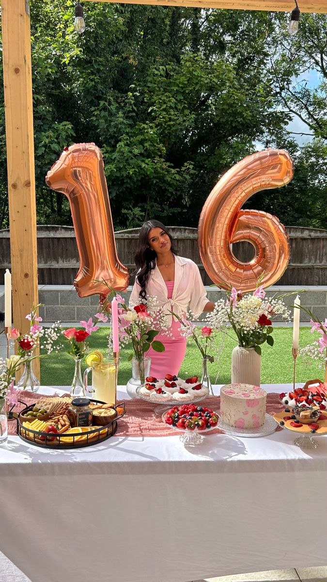 a woman standing in front of a table filled with desserts and balloons that spell out the number six