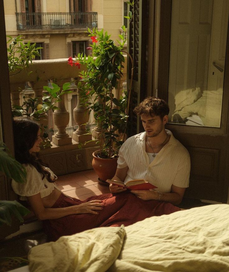 a man and woman sitting on the floor in front of a window with potted plants