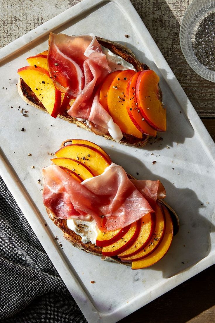 two slices of bread topped with sliced peaches and prosciutto on a white tray