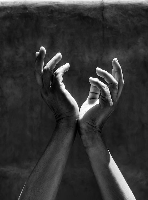 black and white photograph of two hands reaching for each other with their fingers extended in the air