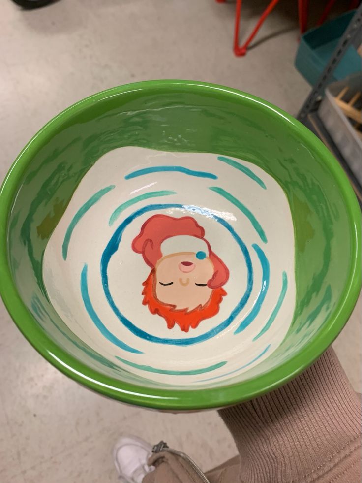 a person holding a green bowl with a drawing on it