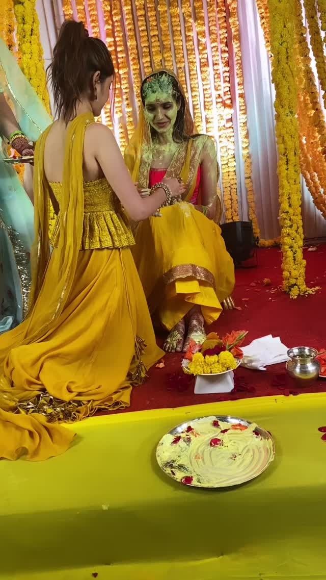 two women dressed in yellow sitting on the ground with food and decorations around them,