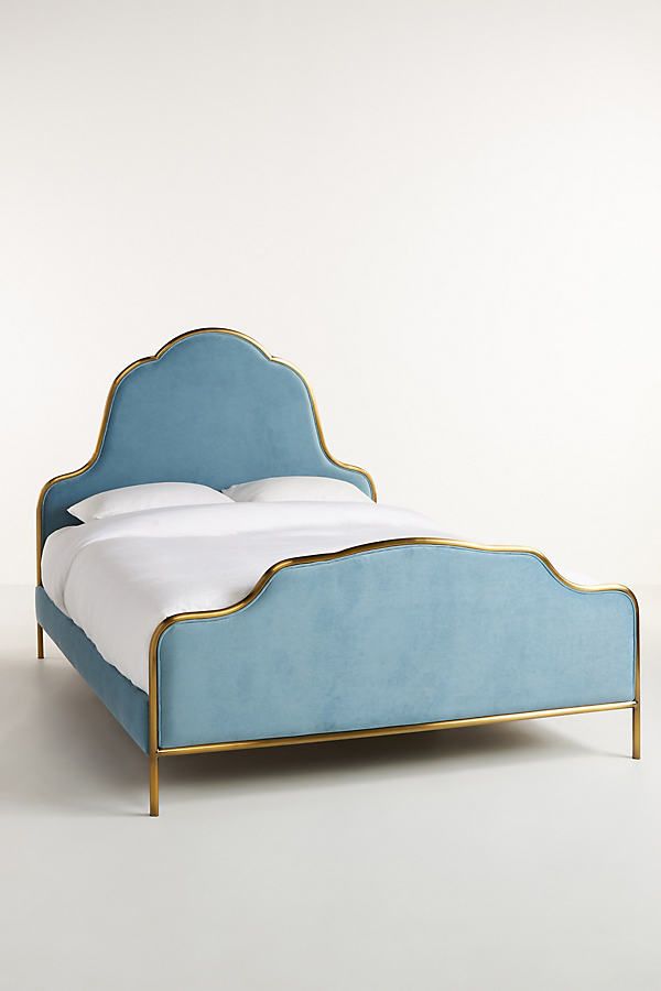 a blue bed with white sheets and gold trim on the headboard is shown in front of a plain background