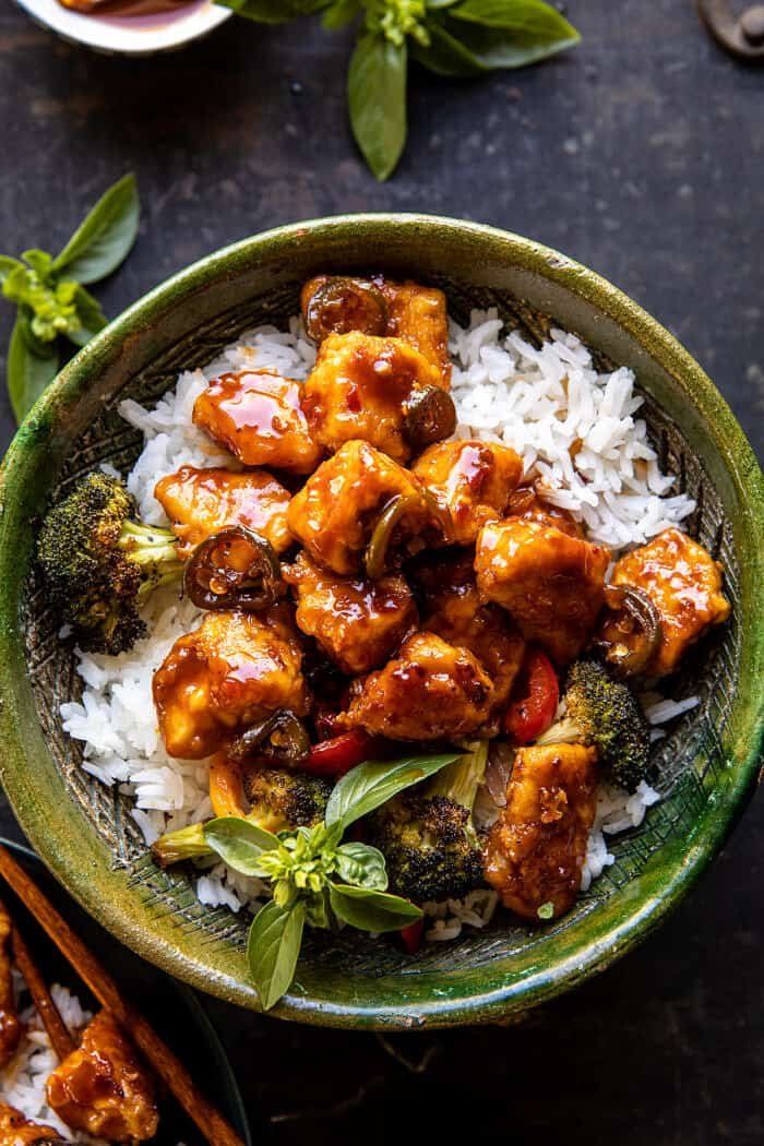 a green bowl filled with chicken and broccoli on top of rice next to chopsticks