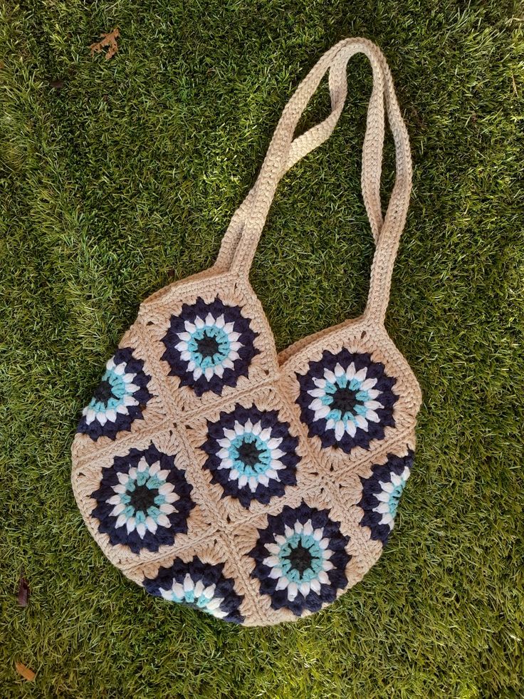 a crocheted bag sitting on top of green grass with blue and white flowers