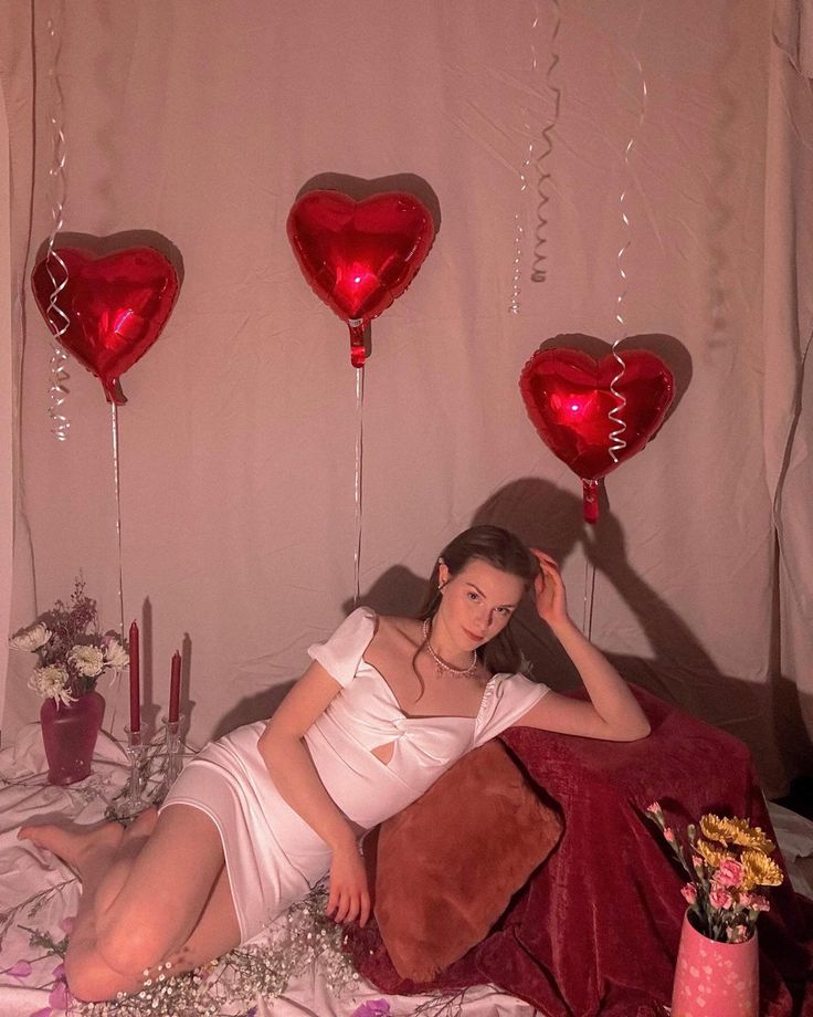 a woman laying on a bed with red heart shaped balloons