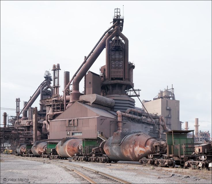 an old factory building with many pipes and machinery on the tracks in front of it