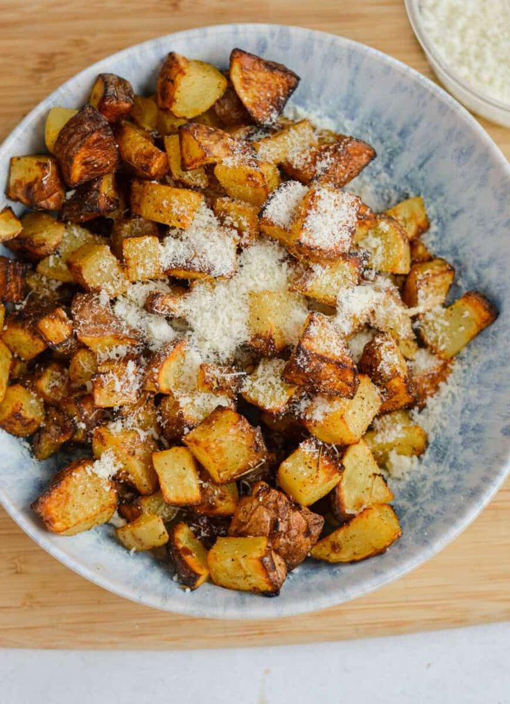 a white bowl filled with cooked potatoes covered in parmesan sprinkles