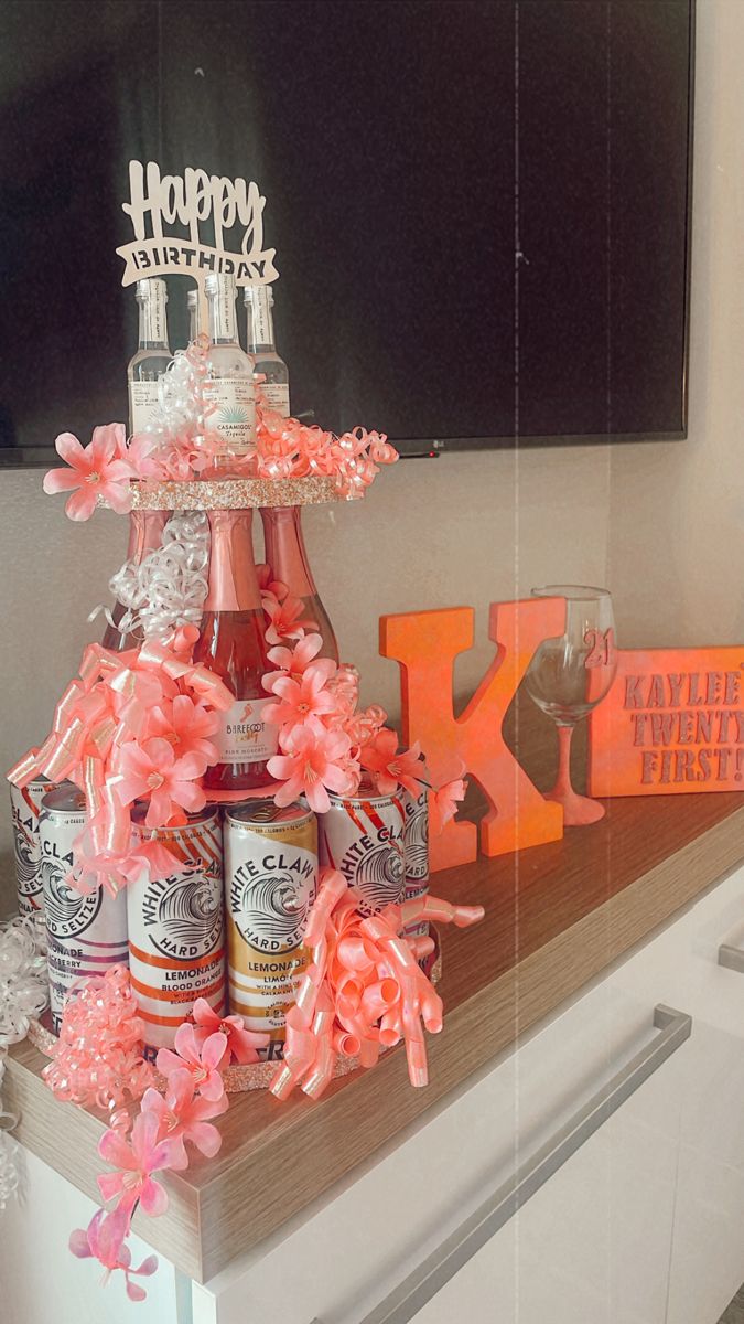 a birthday cake made out of beer bottles and pink flowers on a table with an orange letter