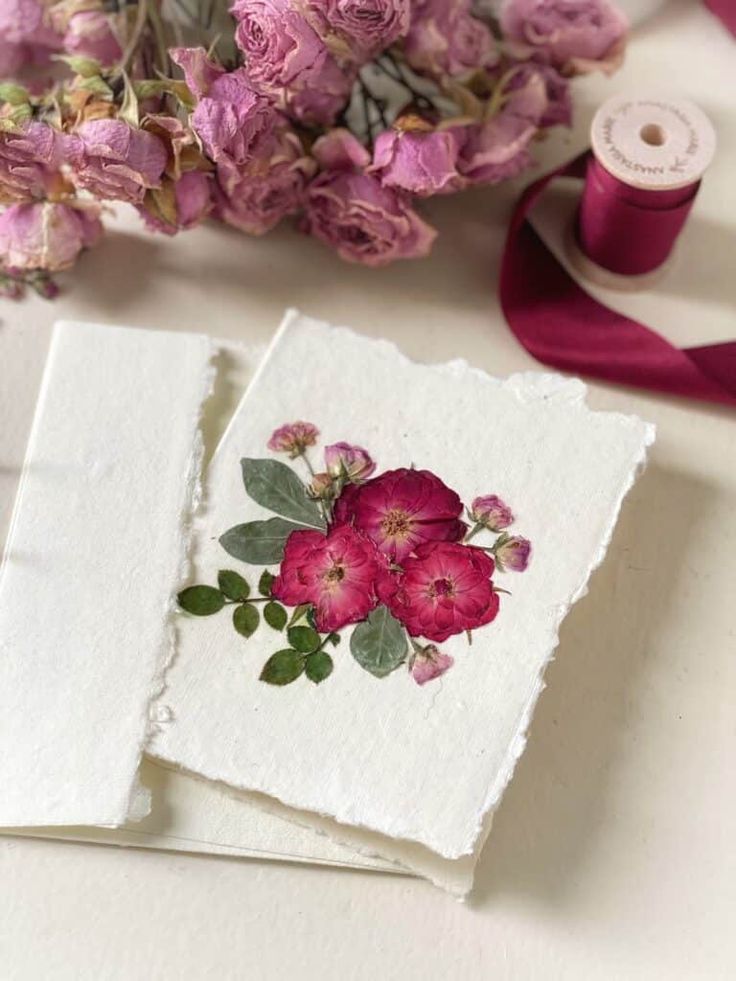 two cards with pink flowers on them next to some spools of red thread