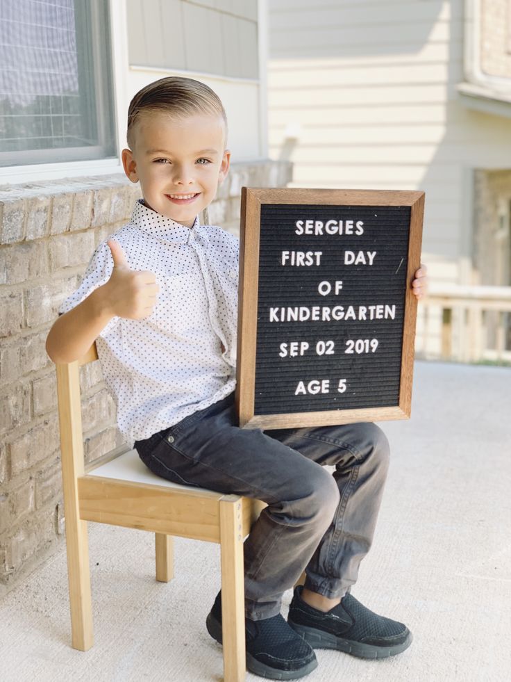 a young boy sitting on a chair holding up a sign