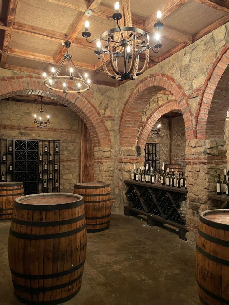 a wine cellar with several wooden barrels and chandeliers