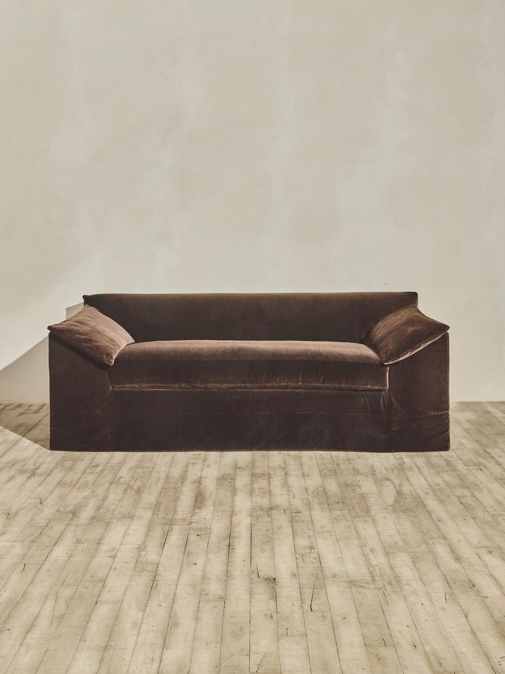 a brown couch sitting on top of a wooden floor next to a white wall in an empty room