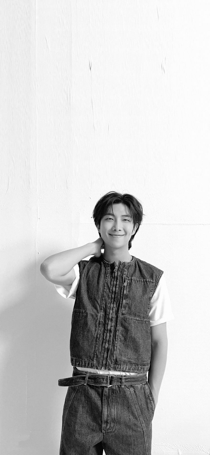 a young man in overalls is smiling and holding his hands on his head while standing against a wall