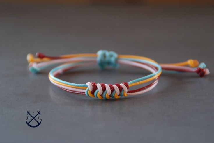 two colorful bracelets sitting on top of a gray table next to an orange, yellow and blue cord