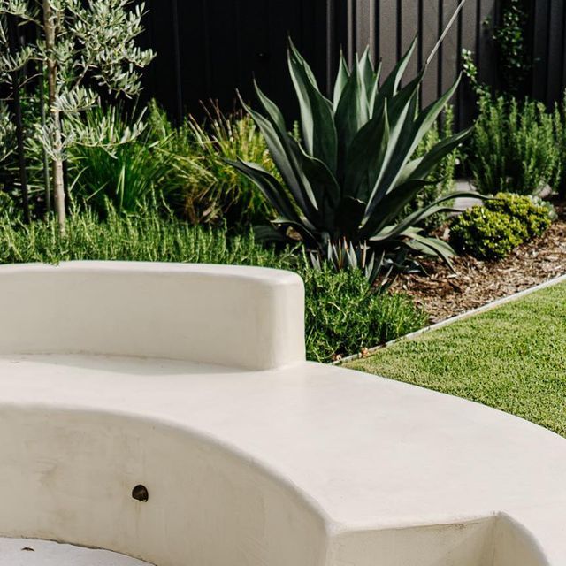 a white bench sitting on top of a lush green field next to a garden filled with plants