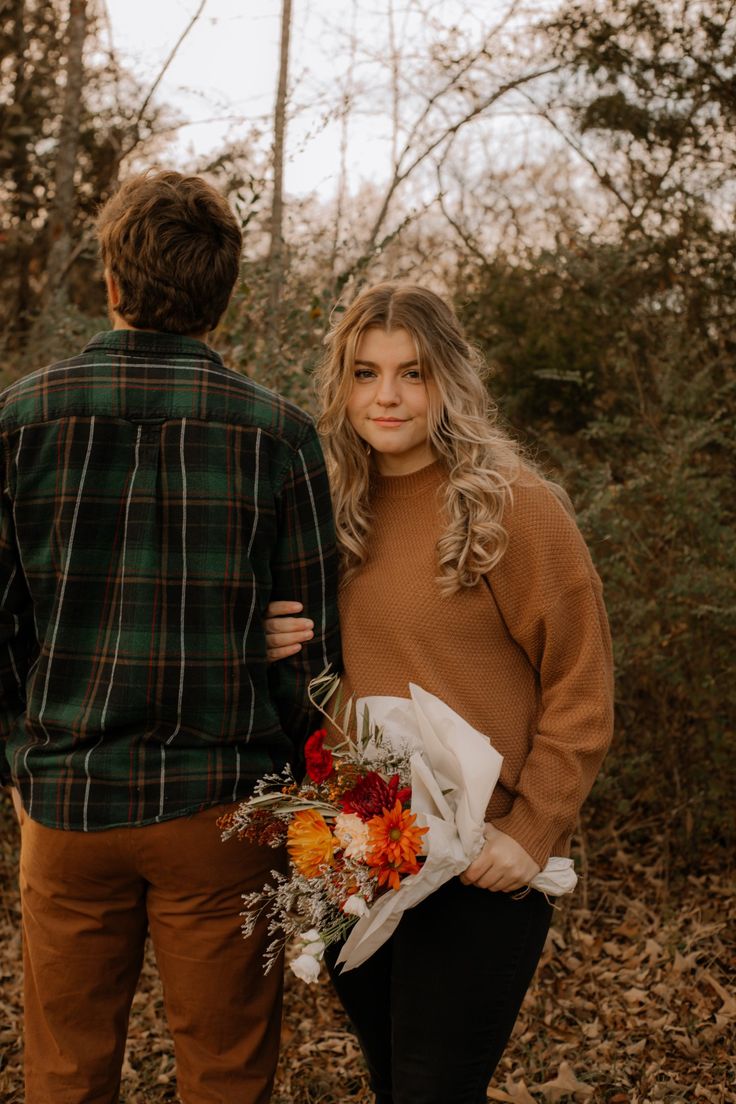 a man and woman standing next to each other in the woods with flowers on their bouquets