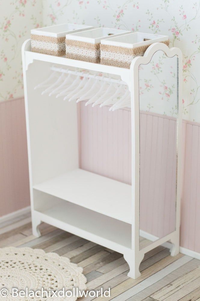 a small white shelf with clothes hanging on it's sides in front of a floral wallpapered wall