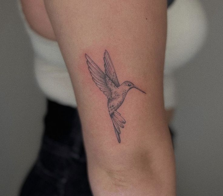 a small tattoo on the arm of a woman with a hummingbird flying above it