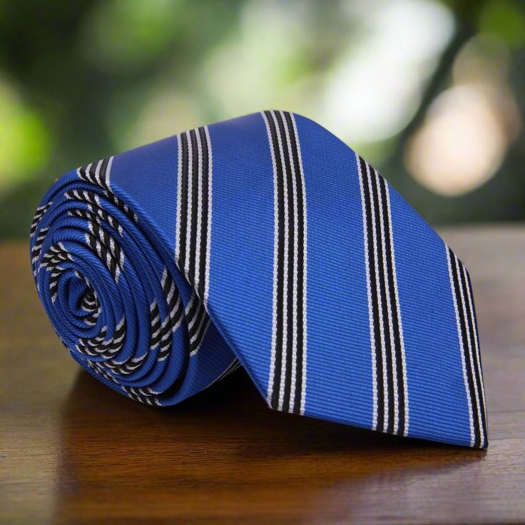 Blue Silk Necktie with White and Black Stripes Pattern This sophisticated blue silk necktie featuring white and black stripes offers a sleek and modern touch to your ensemble. The combination of bold stripes in contrasting colors ensures a stylish and polished appearance. Dress Shirts White Dress Shirt: A classic white shirt provides a crisp backdrop that enhances the blue and striped design of the tie, creating a sharp and clean look ideal for professional and formal settings. Light Grey Dress Classic Blue Ties For Business, Classic Blue Business Ties, Pinstripe Ties For Formal Occasions, Classic Striped Ties For Black Tie Events, Classic Striped Tie For Black Tie Events, Classic Striped Tie For Black Tie Occasions, Dapper Blue Ties For Workwear, Pinstripe Business Tie, Striped Business Neckwear Ties