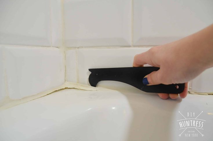 a person using a black handle to clean a bathtub with white tiles on the wall