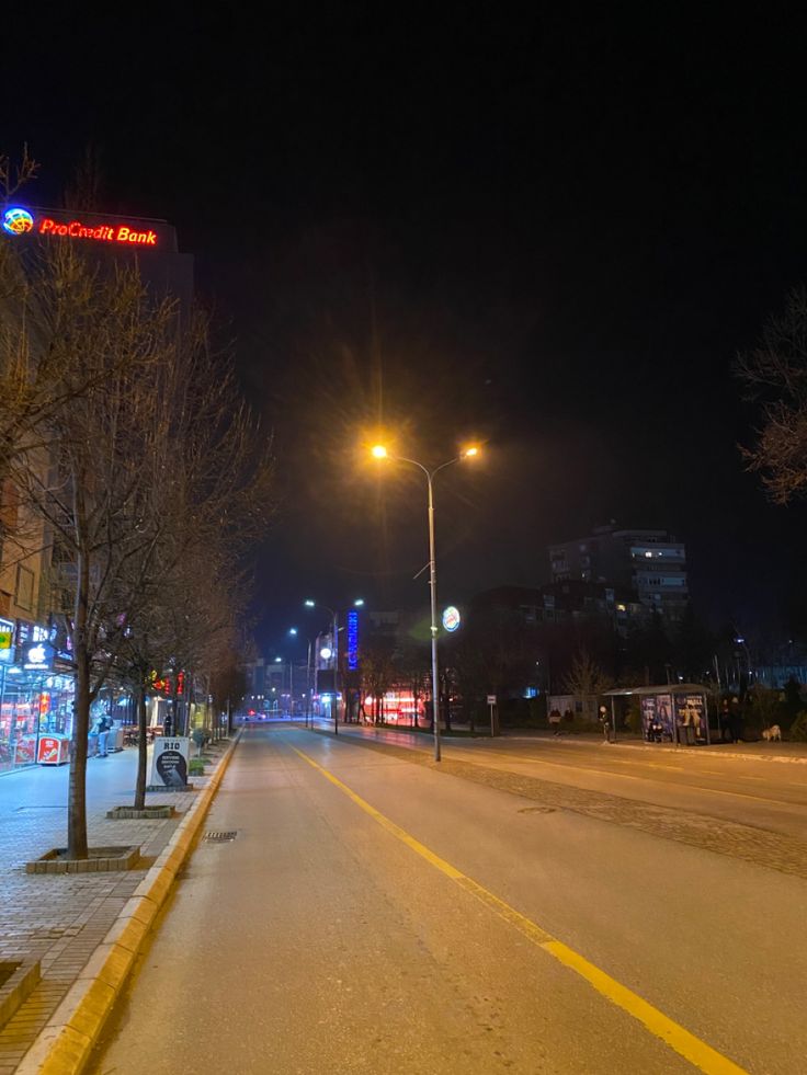 an empty city street at night with no cars on the road and buildings in the background