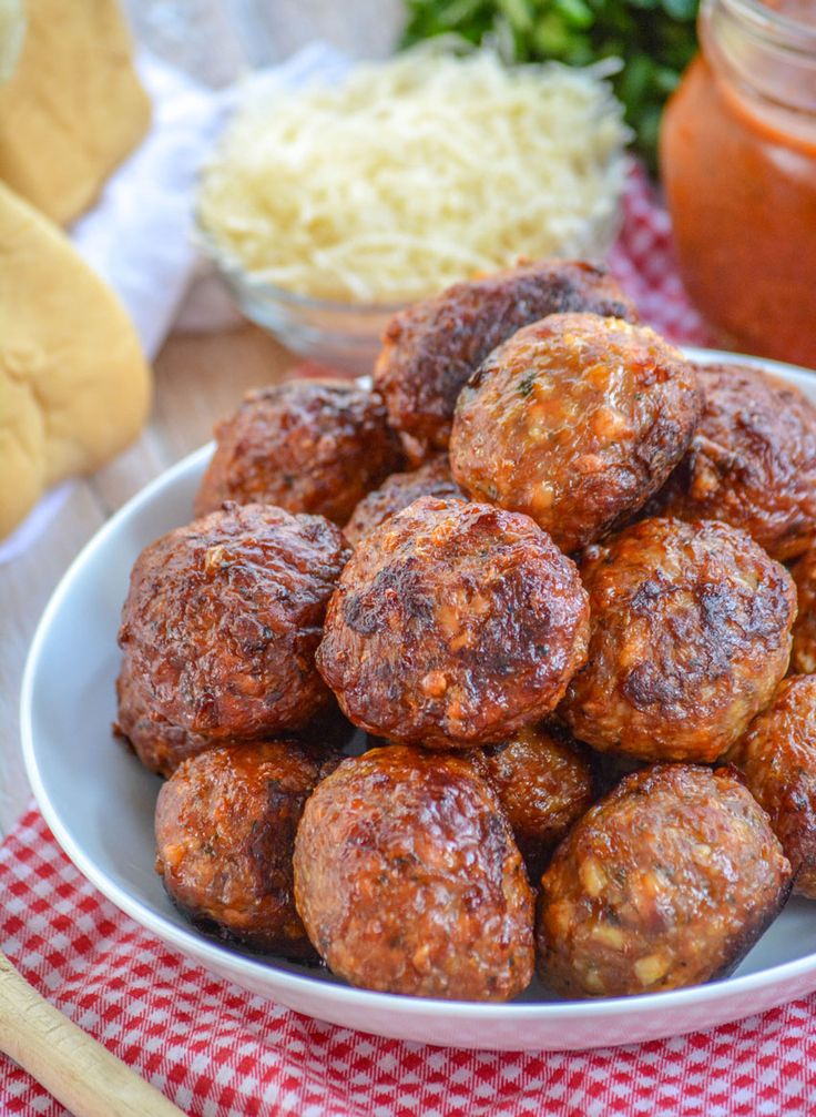 a white bowl filled with meatballs next to some breaded buns on a red and white checkered table cloth