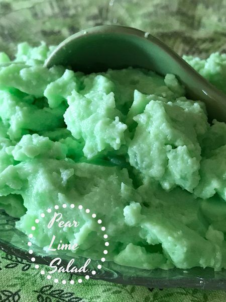 a scoop of green jello sits in a glass bowl with a spoon on it