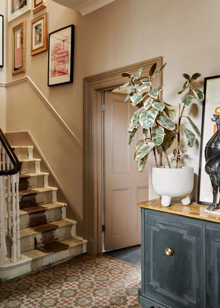 there is a potted plant on the table in front of the stairs and framed pictures