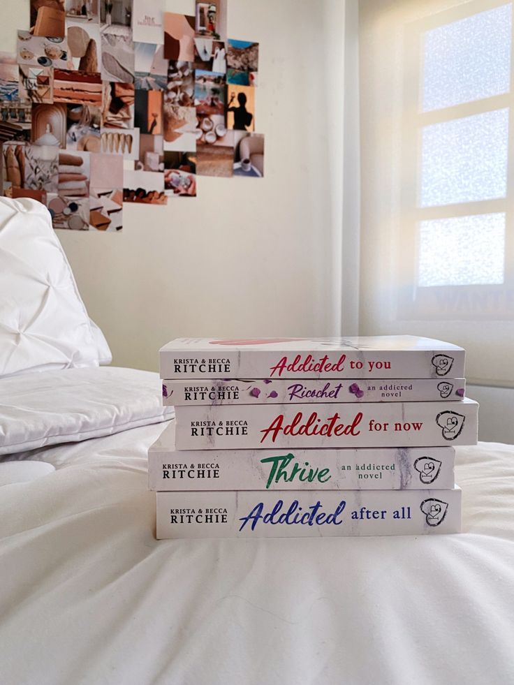 three books stacked on top of each other in front of a bed with white sheets